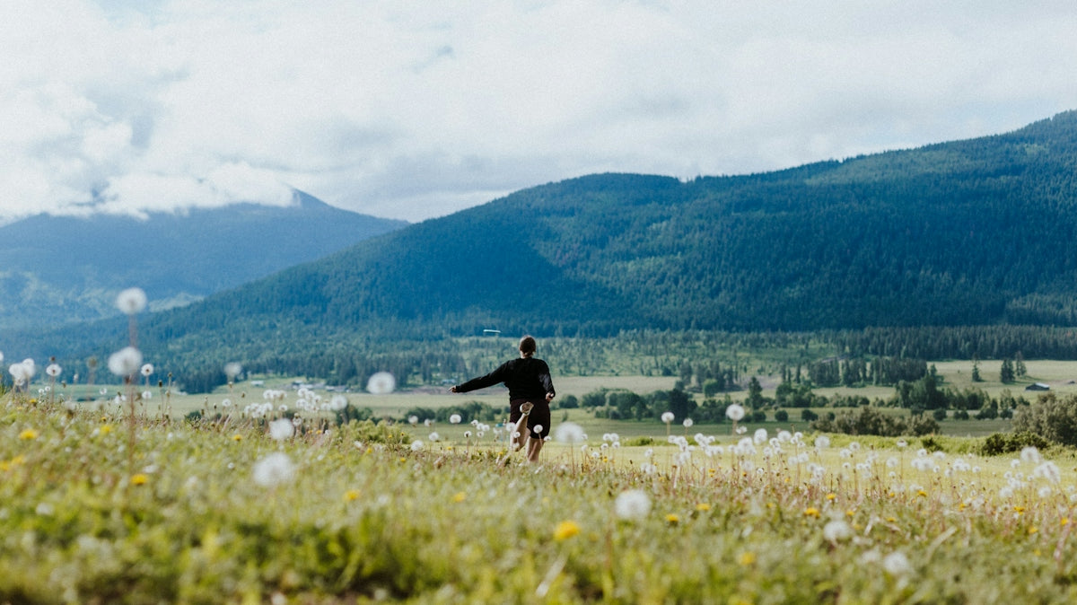 a man is walking through a field with mountains in the background