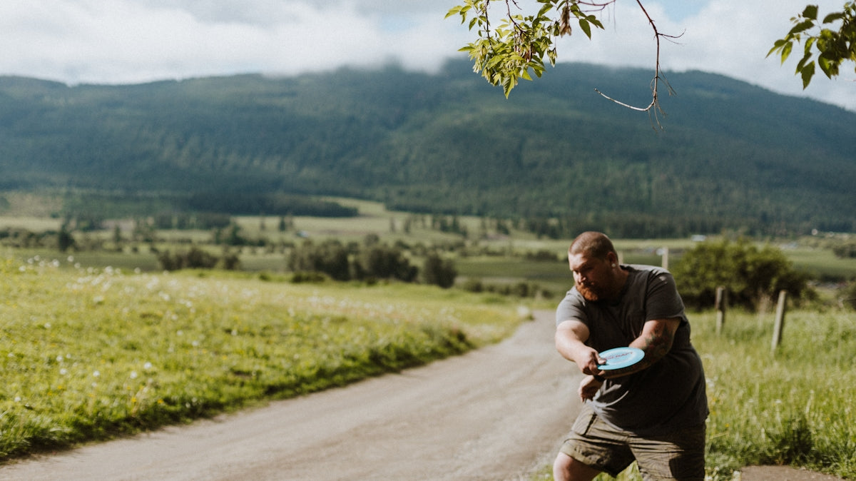 a man throwing a frisbee on a dirt road