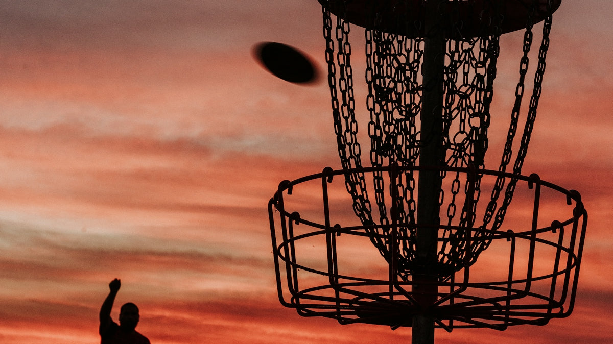 A silhouette of a man throwing a frisbee at a frisbee golf