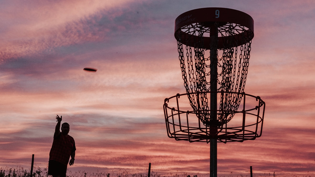 A silhouette of a man throwing a frisbee at a frisbee golf