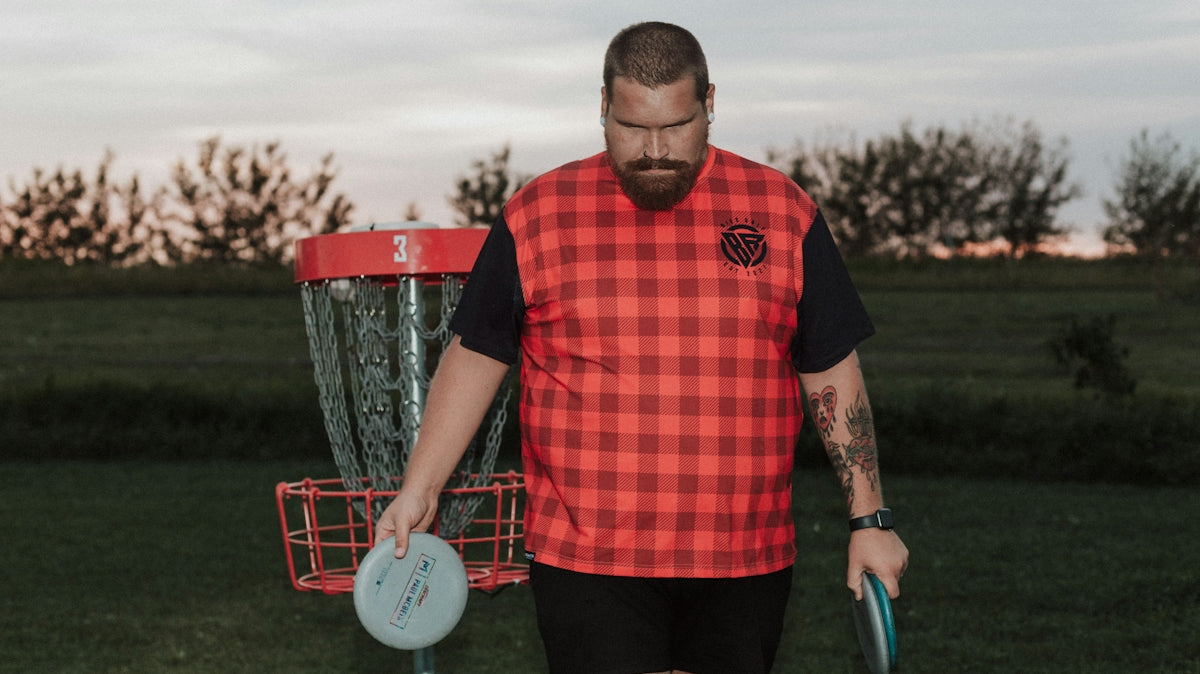 A man holding a frisbee standing next to a frisbee golf net