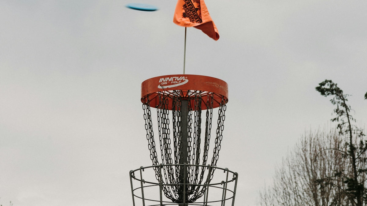 Disc golf basket with a flying disc and orange flag