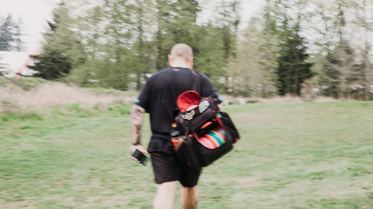 Man carrying a disc golf bag walks across field