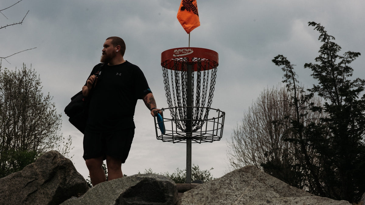 Man walking with disc golf basket and flag