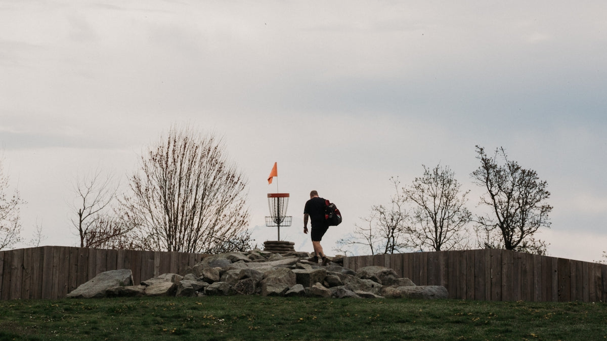 Man walking towards a disc golf basket on a hill.
