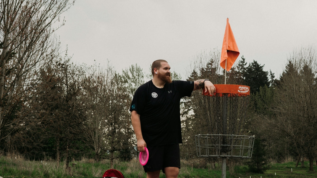 Man standing by disc golf basket with disc and bag