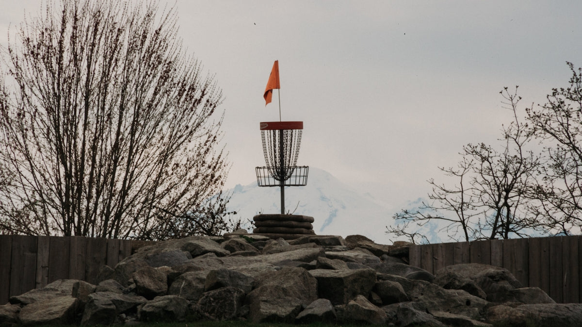 Disc golf basket with orange flag on rocky mound.