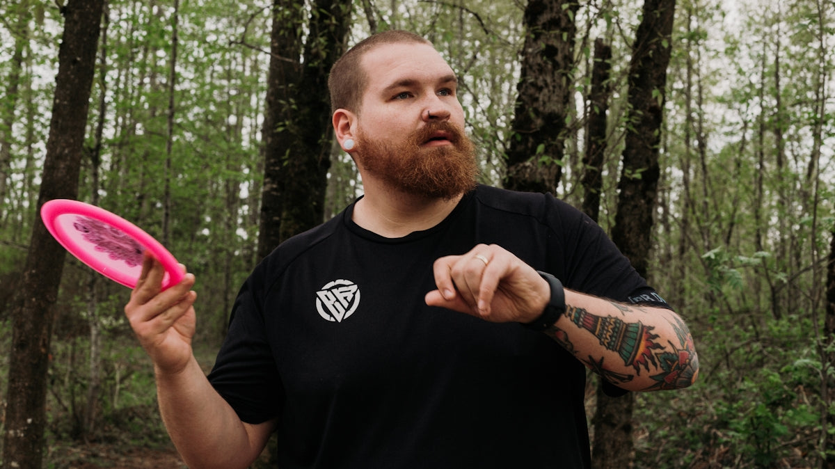 Man holding pink disc golf disc in forest