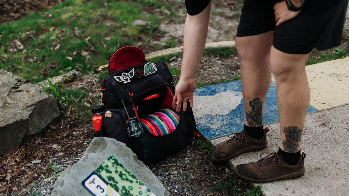 Person reaching for disc golf bag next to course map