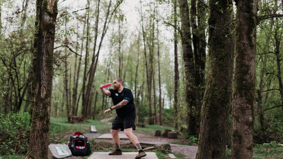 Man throwing a disc golf disc in a wooded park
