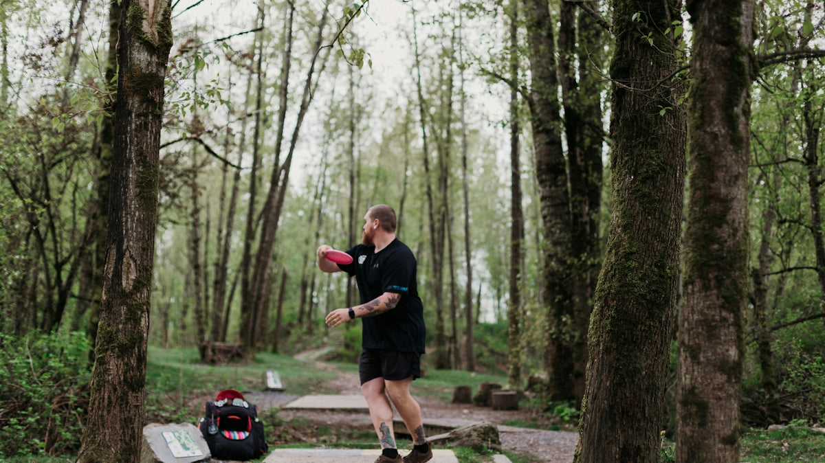 Man throwing a disc golf disc in a wooded park