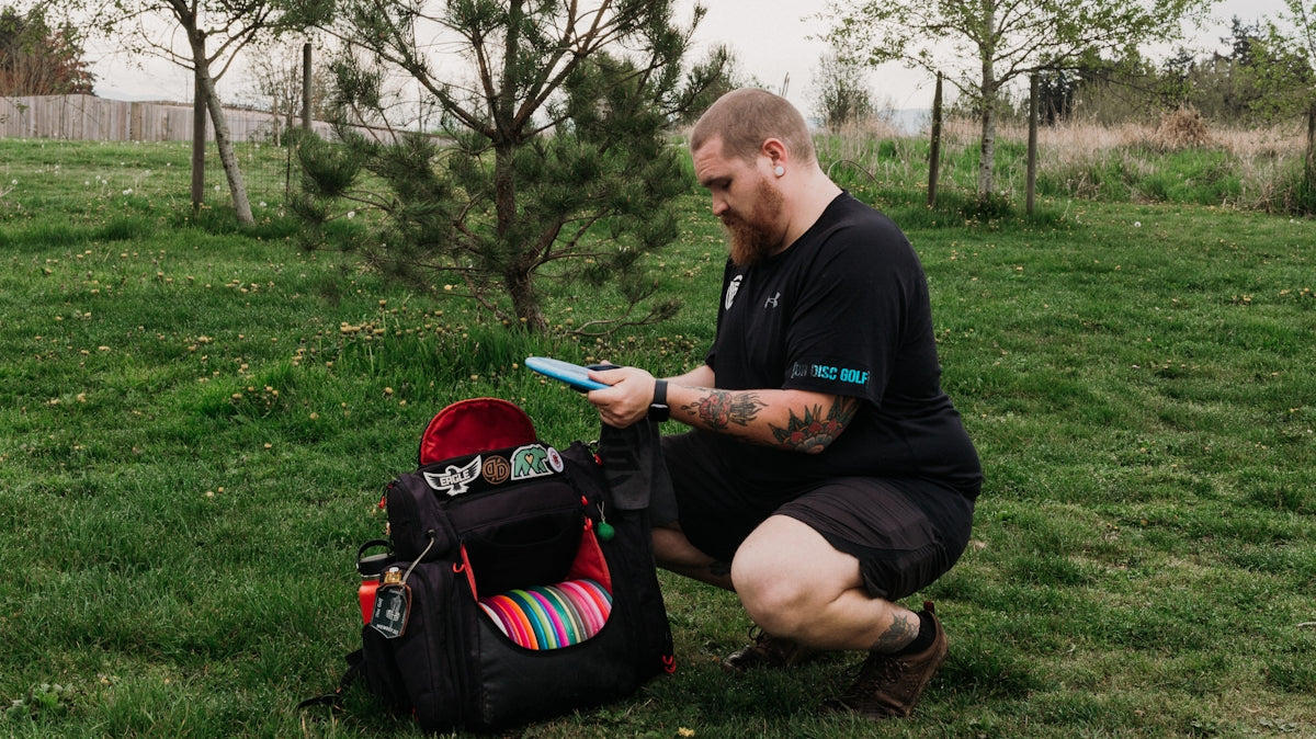Man with disc golf bag in grassy field.