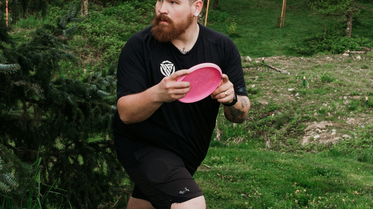 Man throwing a pink disc golf disc in a park.