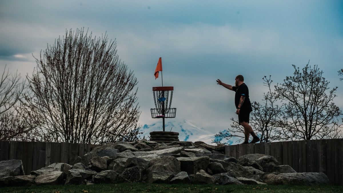 Man throwing disc golf disc towards basket on course
