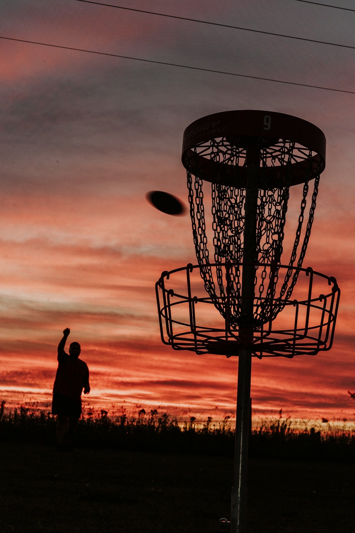 A silhouette of a man throwing a frisbee at a frisbee golf