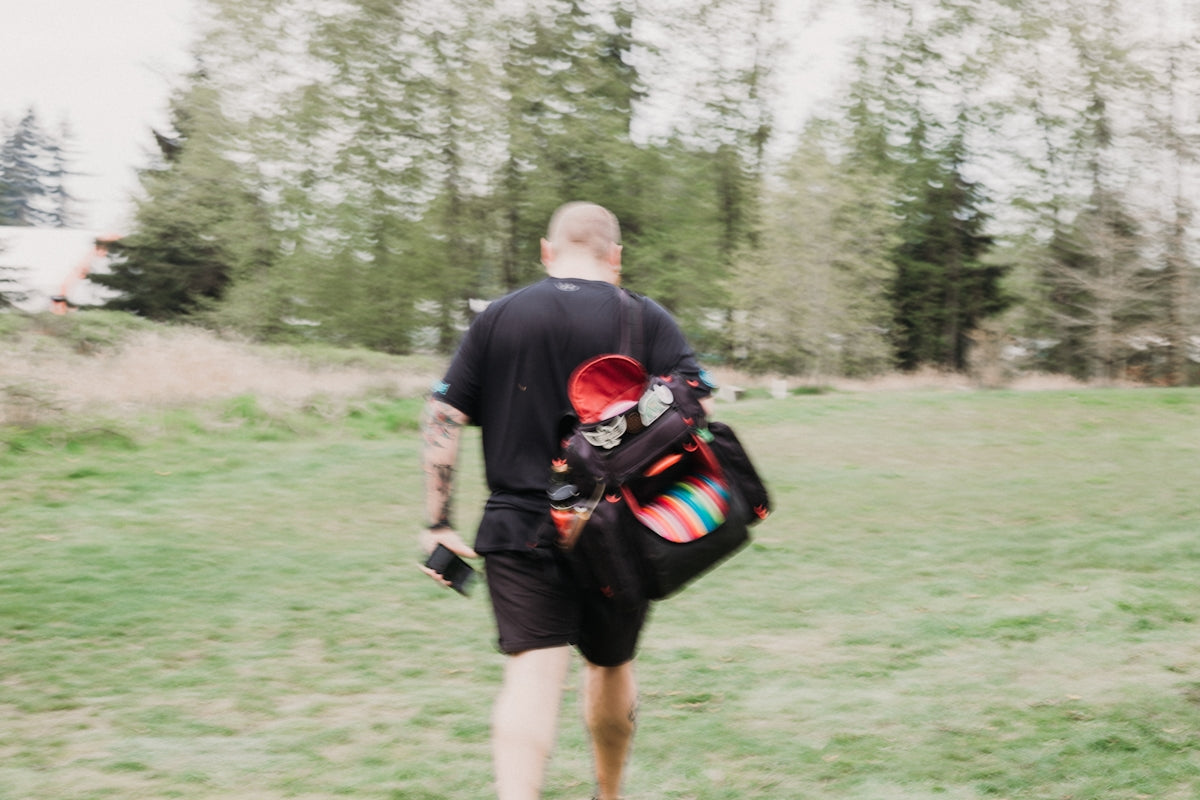 Man carrying a disc golf bag walks across field