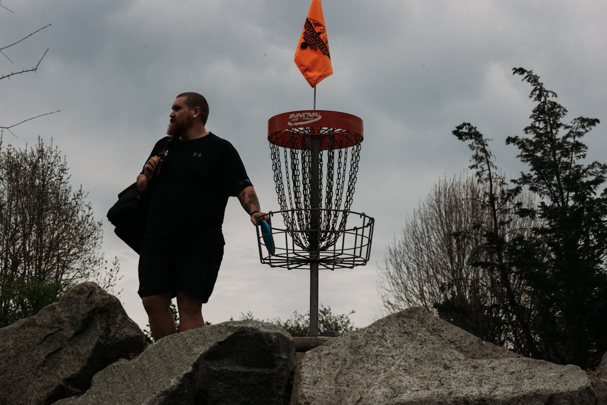 Man walking with disc golf basket and flag