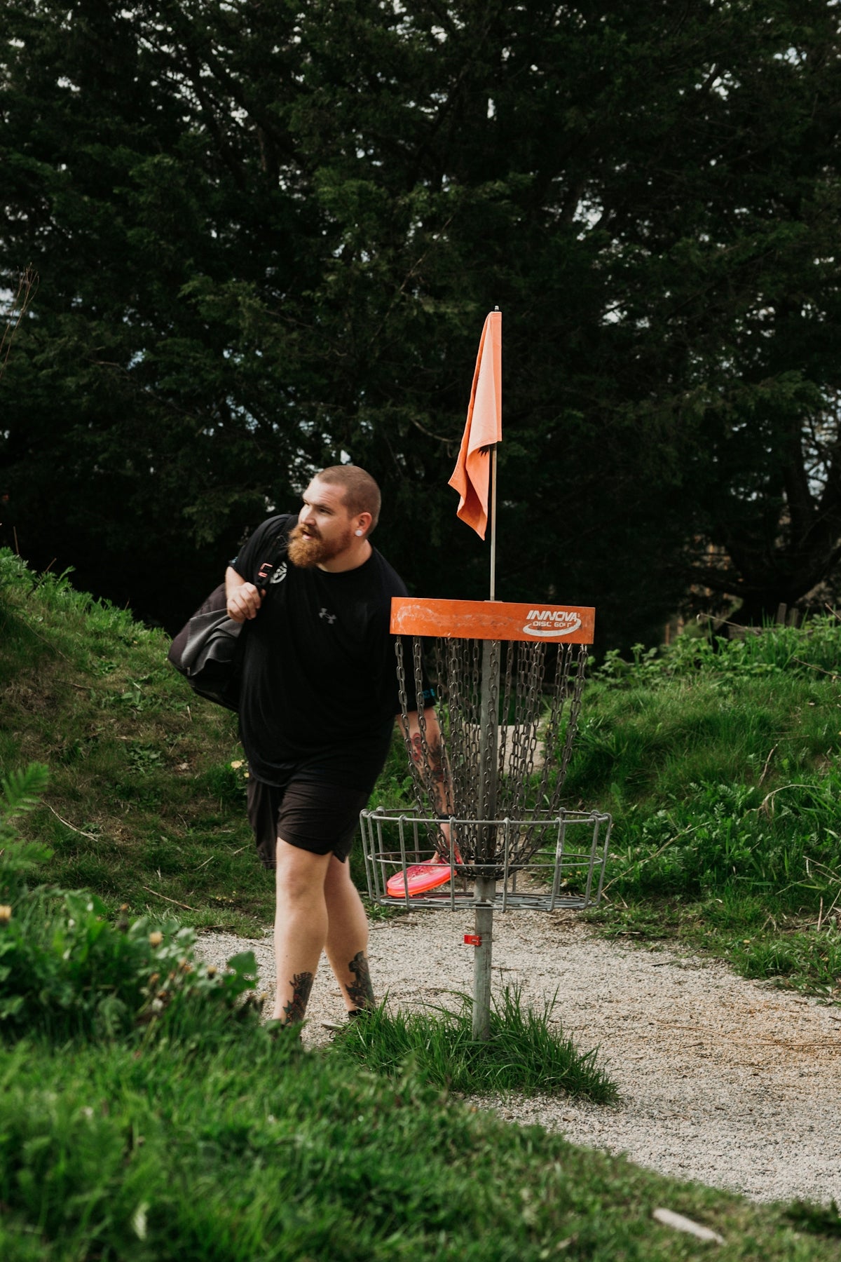 Man walking past a disc golf basket with a bag.
