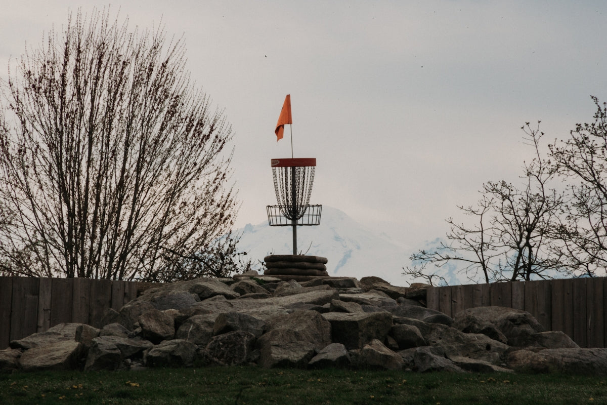 Disc golf basket with orange flag on rocky mound.