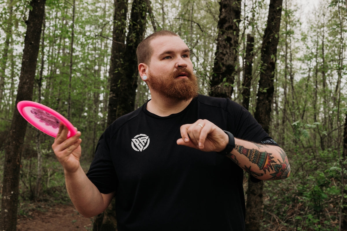 Man holding pink disc golf disc in forest