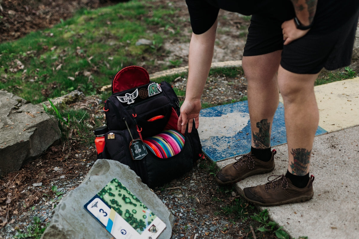 Person reaching for disc golf bag next to course map