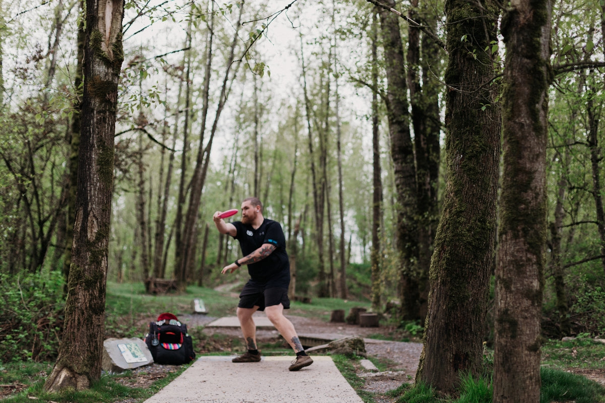 Man throwing a disc golf disc in a wooded park