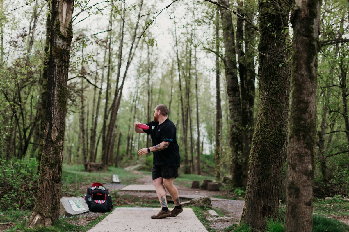 Man throwing a disc golf disc in a wooded park