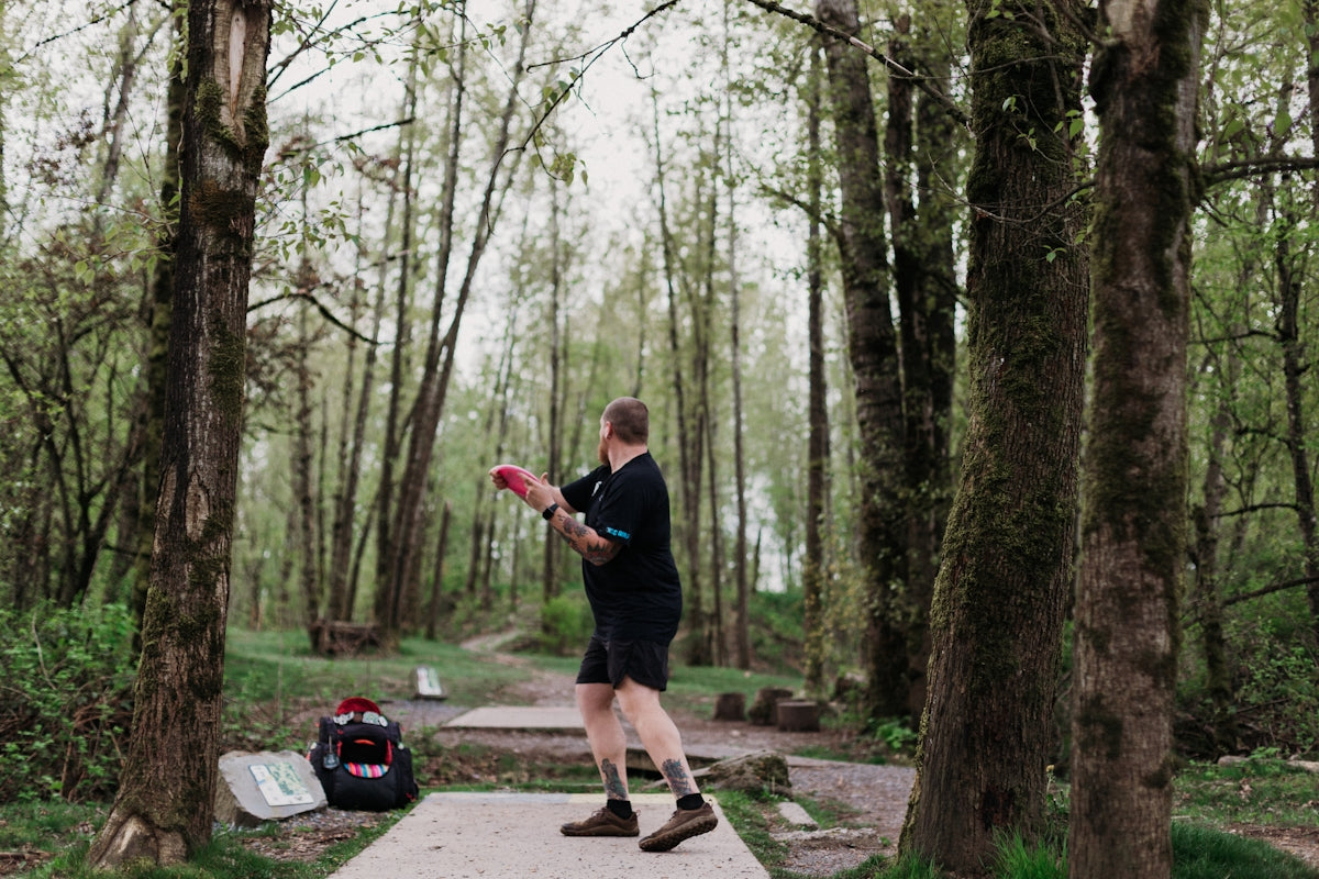 Man throwing a disc golf disc in a wooded park.